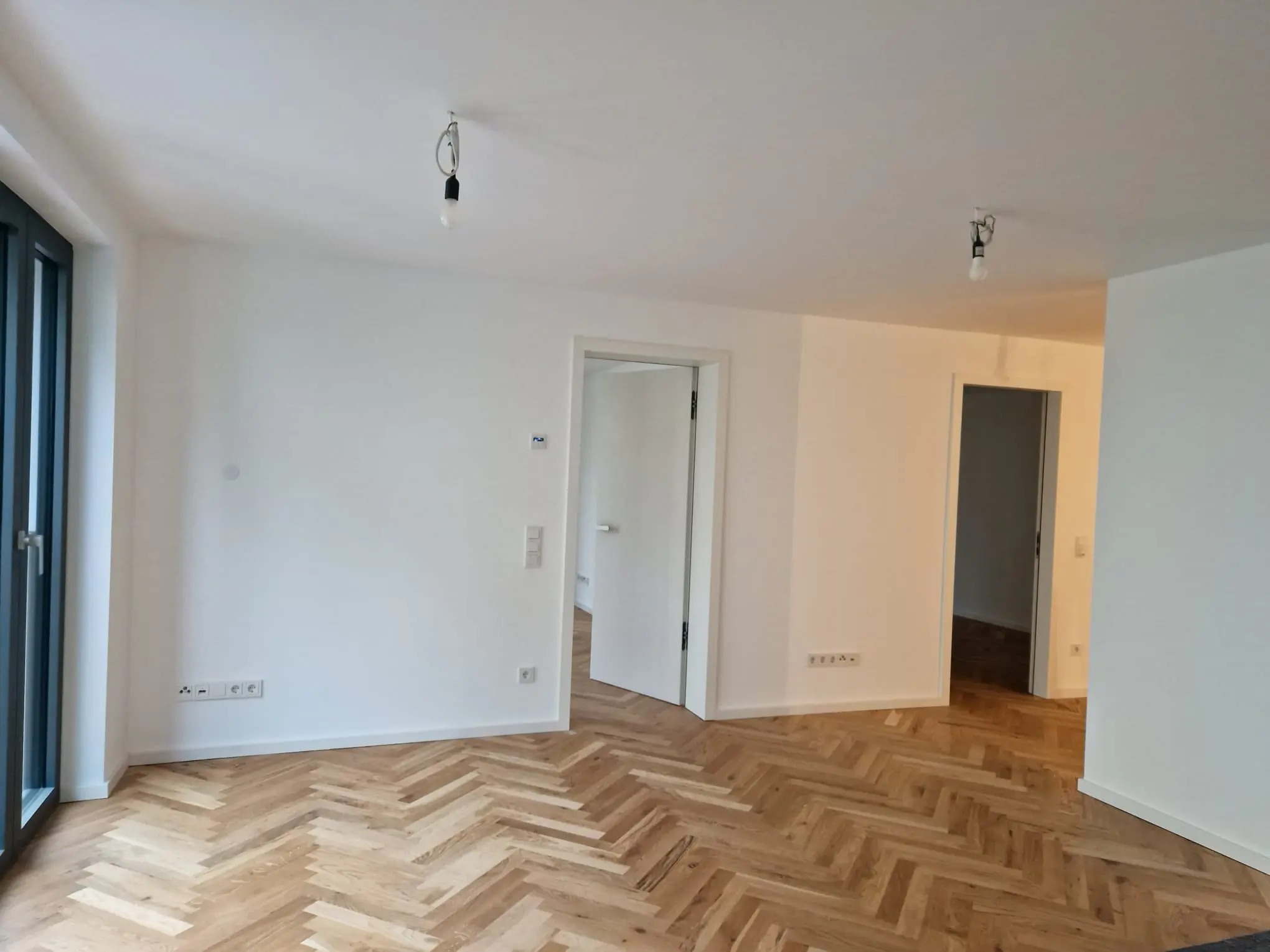 Heller Wohnraum mit Fischgrätparkett und raumhohen Fenstern
