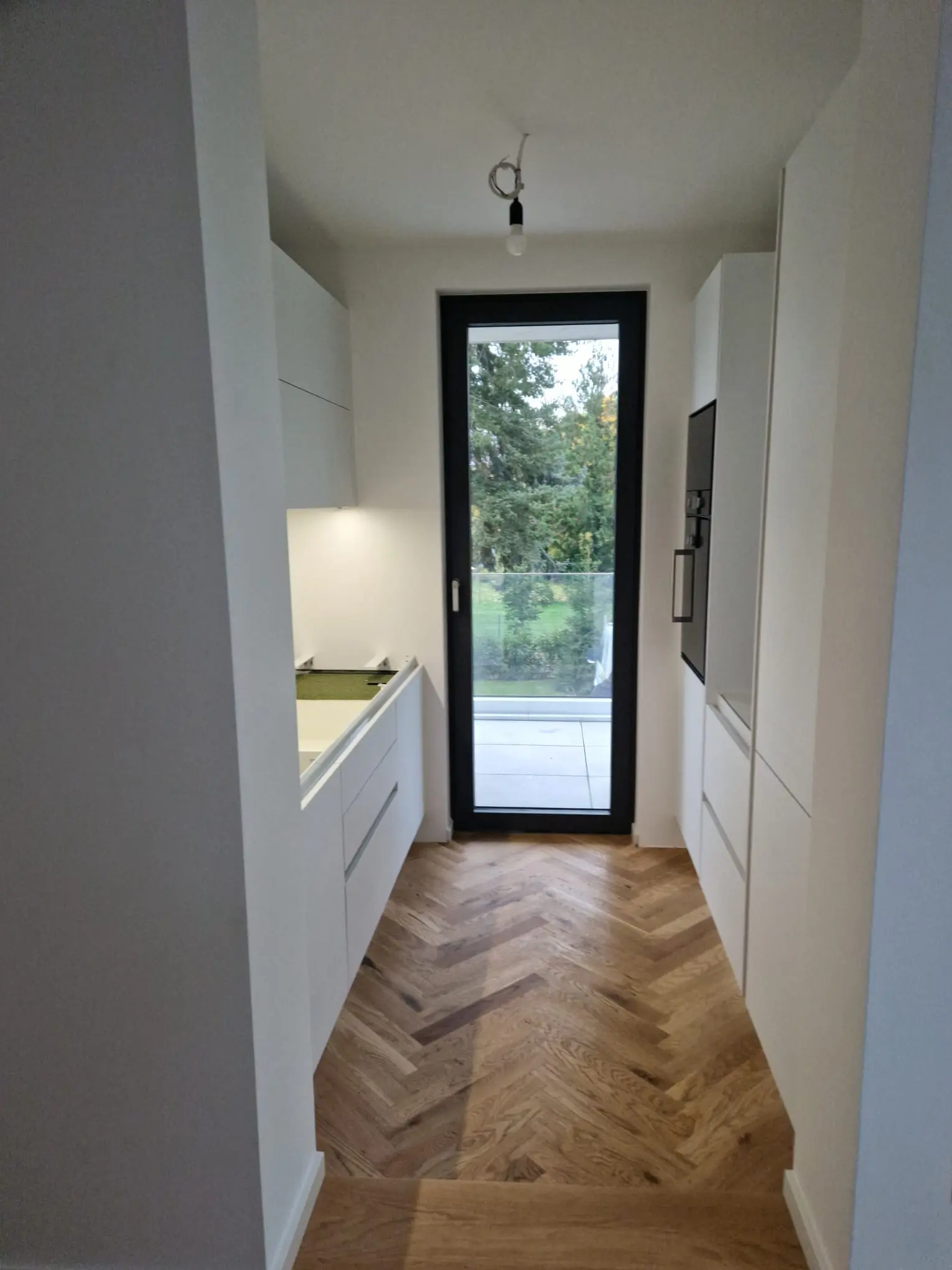 Maßgefertigte weiße Küche mit Fischgrätparkett und raumhohem Fenster